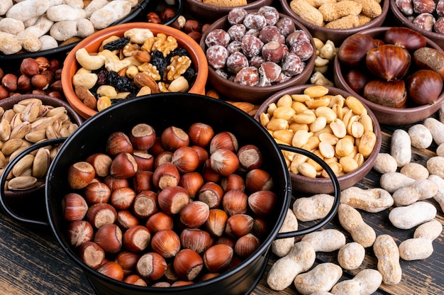 Einige verschiedene Nüsse und getrocknete Früchte mit Pekannuss, Pistazien, Mandeln, Erdnüssen, Cashewnüssen, Pinienkernen in verschiedenen Schalen und einer schwarzen Pfanne