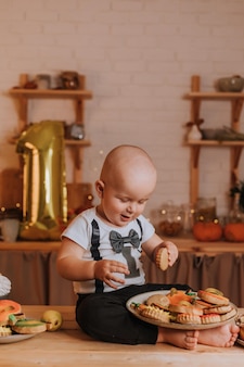 Einjähriges baby isst hausgemachten bemalten lebkuchen. ersten geburtstag in festlicher atmosphäre. gesunder snack für kinder. kleiner junge sitzt am küchentisch. foto in hoher qualität