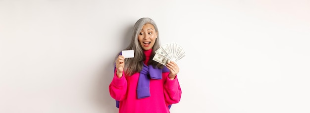 Kostenloses Foto einkaufskonzept glückliche asiatische seniorin, die erstaunt auf die kreditkarte blickt und gelddollarst zeigt