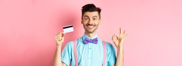 Kostenloses Foto einkaufskonzept lächelnder, gutaussehender männlicher käufer, der ein ok-zeichen und eine plastikkreditkarte zeigt, die etwas kauft