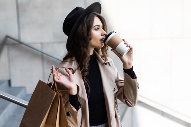 Einkaufstag. Kaffeepause. Attraktive junge Frau mit Papiertüten, die auf Stadtstraße gehen.