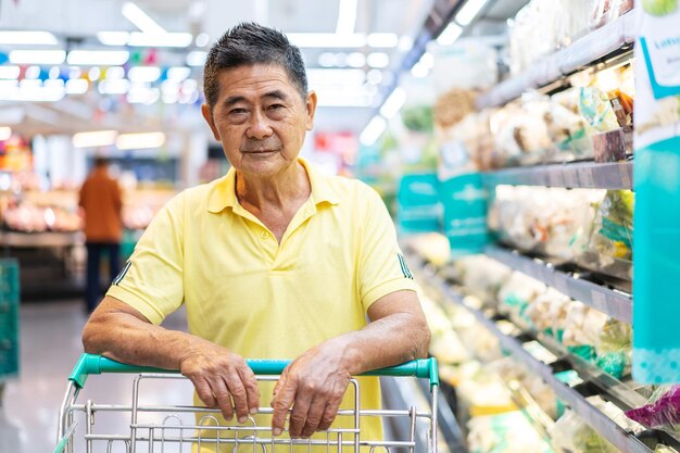 Einkaufswagen des asiatischen Seniors, der andere Produkte im Supermarkt auswählt