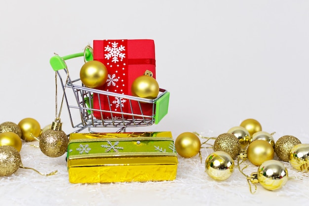 Einkaufswagen mit Geschenkboxen und goldenen Kugeln auf einer Schneeflocke auf einem weißen Hintergrund