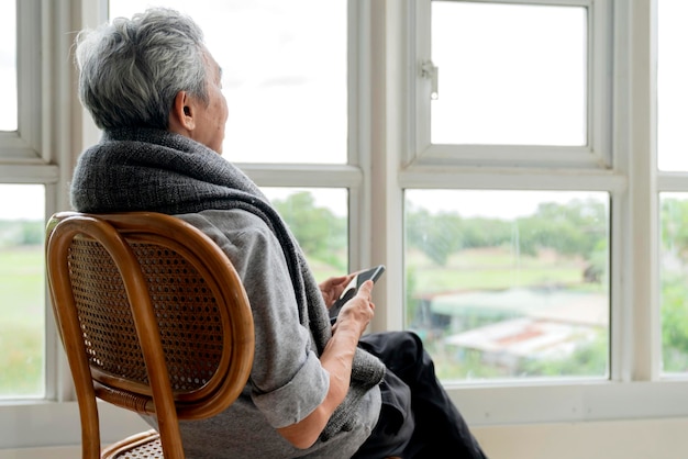 Einsamer älterer älterer Mann, der genießt, aus dem Fenster zu Hause zu schauen, von seinem Fenster aus Seitenansicht eines älteren Mannes, der an einer chronischen Alzheimer-Krankheit leidet und in einem Wohnzimmer sitzt