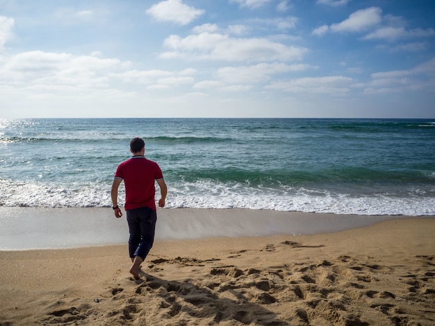 Einsamer Mann, der auf dem Strand unter dem schönen bewölkten Himmel geht