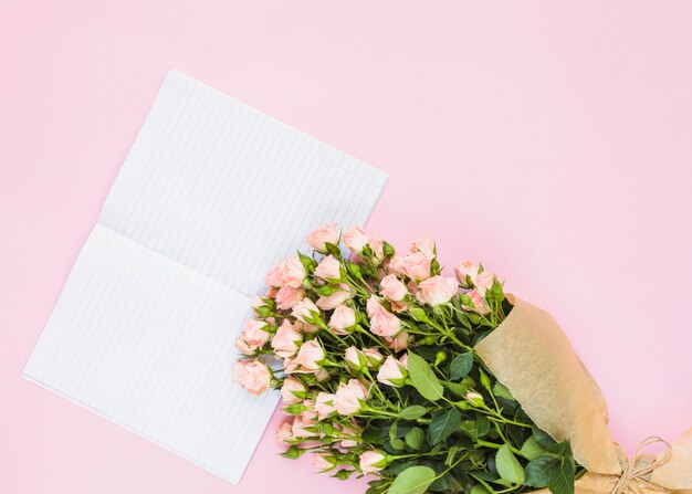 Einzeiliges Seitennotizbuch und Rosenblumenstrauß auf rosa Hintergrund