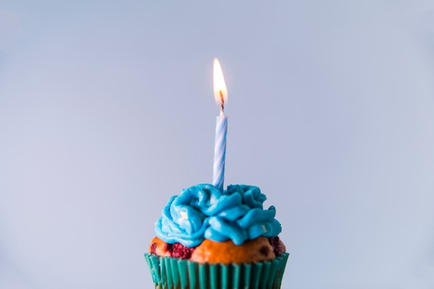 Einzelne brennende Kerze über dem kleinen Kuchen gegen blauen Hintergrund