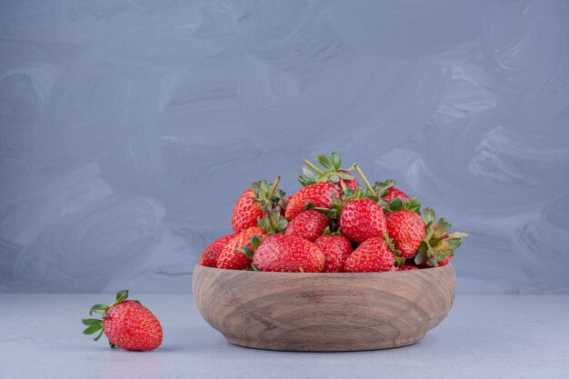 Einzelne Erdbeere neben einer hölzernen Schüssel Erdbeeren auf Marmorhintergrund.