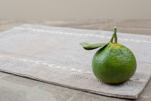 Einzelne frische Mandarine auf grauer Tischdecke.