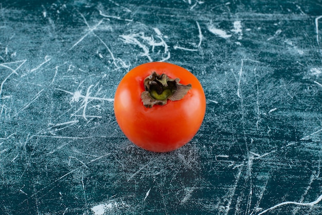 Einzelne frische Persimone auf Marmortisch.