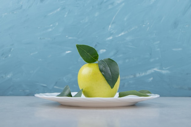 Einzelner Apfel mit Blättern auf weißem Teller.