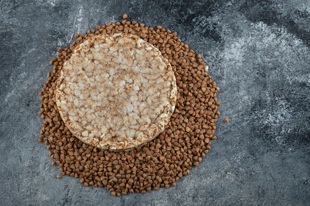 Kostenloses Foto einzelner reiskuchen und ungekochter buchweizen auf marmoroberfläche