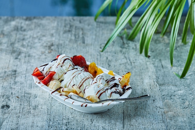 Eis mit Erdbeere, Banane, Orange auf dem weißen Teller mit Löffel