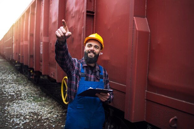 Eisenbahnarbeiter-Supervisor, der die Fracht überprüft und auf einen der Güterzugwagen zeigt