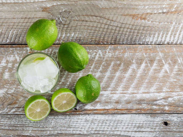 Kostenloses Foto eisiger mojito-cocktail in einer glasschale mit limetten lag flach auf einer holzoberfläche