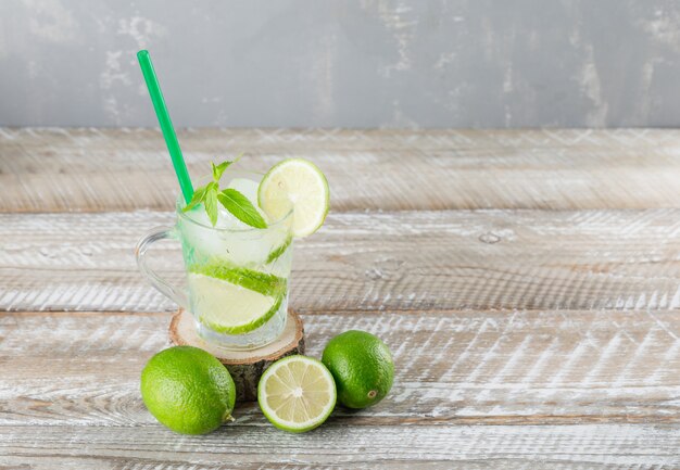 Eisiger Mojito-Cocktail mit Limetten, Minzstroh in einer Tasse auf Holz- und Gipshintergrund, hohe Winkelansicht.