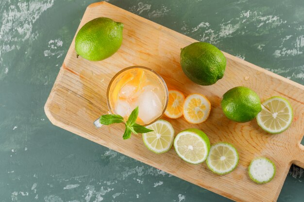 Eisiges Entgiftungswasser mit Orange, Limetten, Minze, Schneidebrett in einer Tasse auf Gips, Draufsicht.