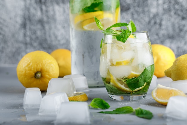 Eisiges Entgiftungswasser mit Zitronen, Minze in Glas und Flasche auf grauer und schmuddeliger Oberfläche