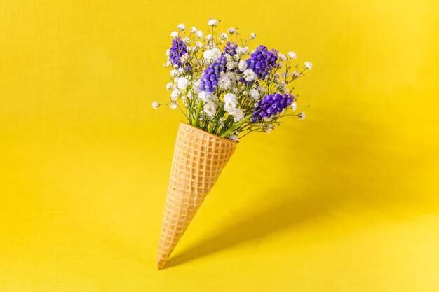 Eistüte mit Blumen auf gelber Wand. Seitenansicht, Kopierraum, Frühlingsblumenkonzept