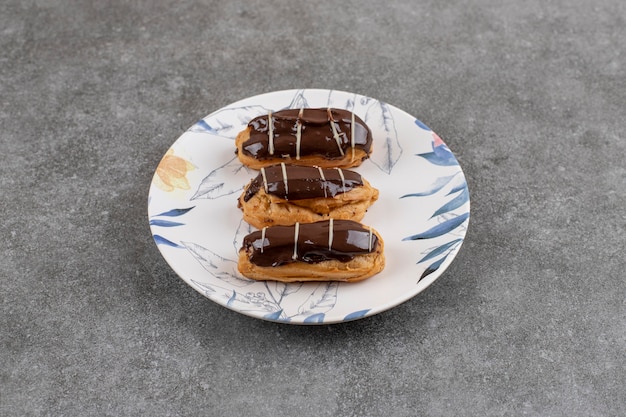 Ekler-Nudeln-Schokoladen-Donut auf weißem Teller über grauer Oberfläche.