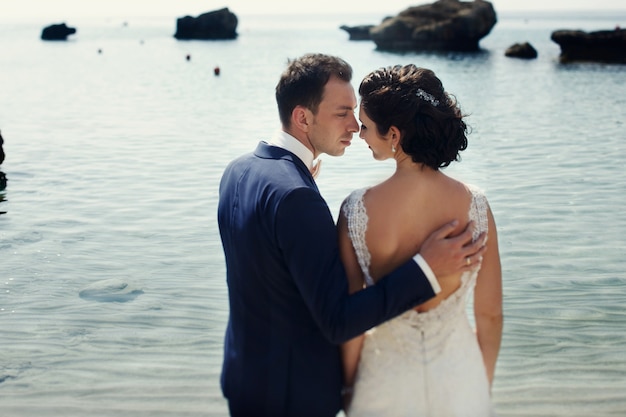 Elegant lächelnde junge Braut und Bräutigam zu Fuß am Strand