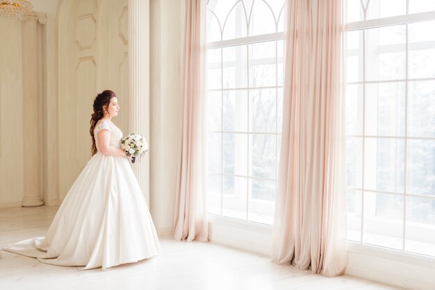 Elegante Braut, die durch ein Fenster schaut