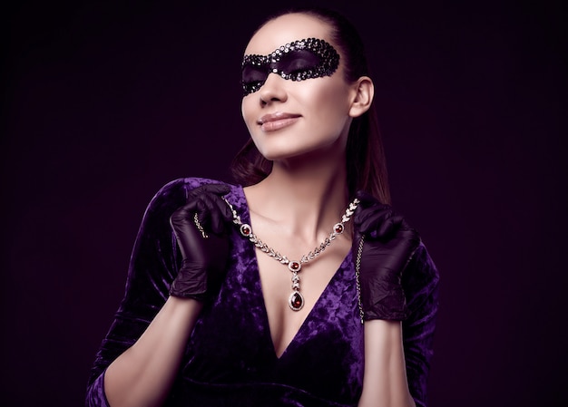 Elegante brünette Frau im schönen lila Kleid, Paillettenmaske und schwarzen Handschuhen