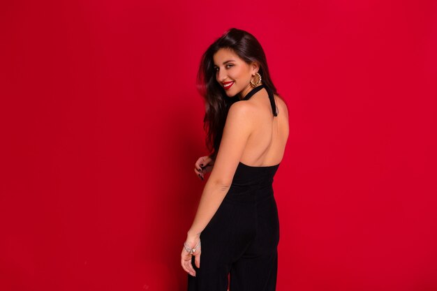 elegante charmante Frau, die schwarzes Kleid mit nacktem Rücken trägt, der über roter Wand aufwirft