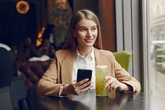 Elegante Frau, die am Tisch mit Cocktail und Telefon sitzt
