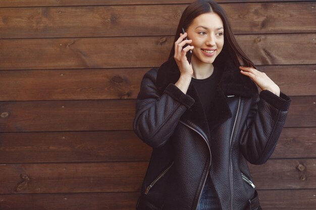 Elegante Frau in einer schwarzen Jacke, die auf einer braunen Wand steht