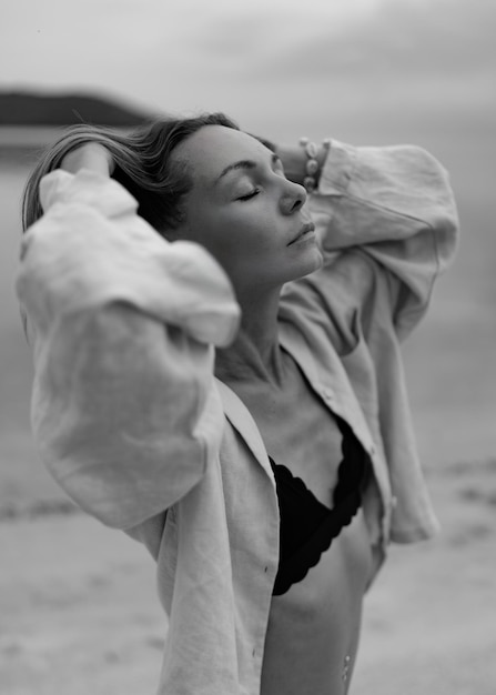 Kostenloses Foto elegante frau in lässigem outfit posiert am einsamen strand bei bewölktem wetter schwarz und weiß