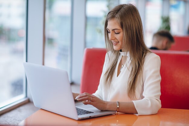 Elegante Frau mit dem Gesicht auf ihrem Laptop schreibt lächelnd