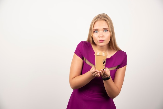 Elegante frau mit tasse kaffee, die auf weißer wand steht.