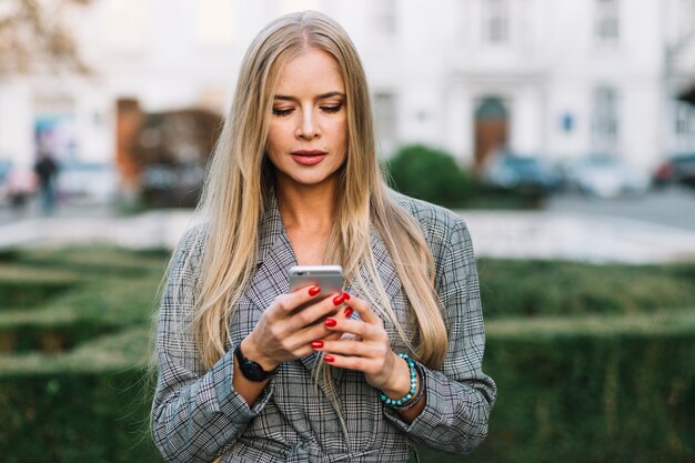 Elegante Geschäftsfrau, die Smartphone in der Stadt betrachtet