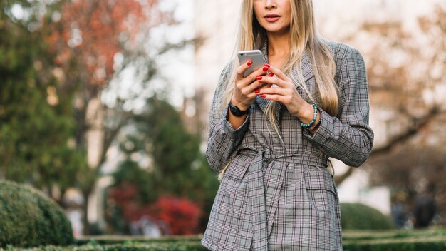 Elegante Geschäftsfrau, die Smartphone in der Stadt betrachtet