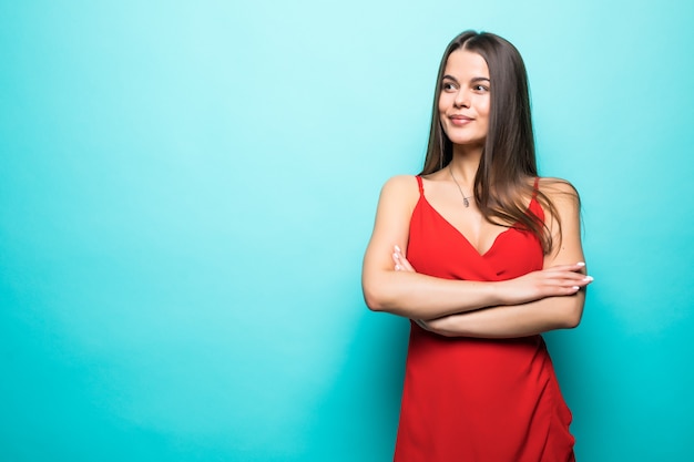 Elegante junge attraktive Frau, die rotes Sommerkleid mit gekreuzten Händen über pastellblauer Wand isoliert trägt.