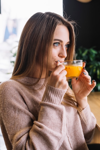 Elegante junge durchdachte Frau, die vom Cup im Café trinkt