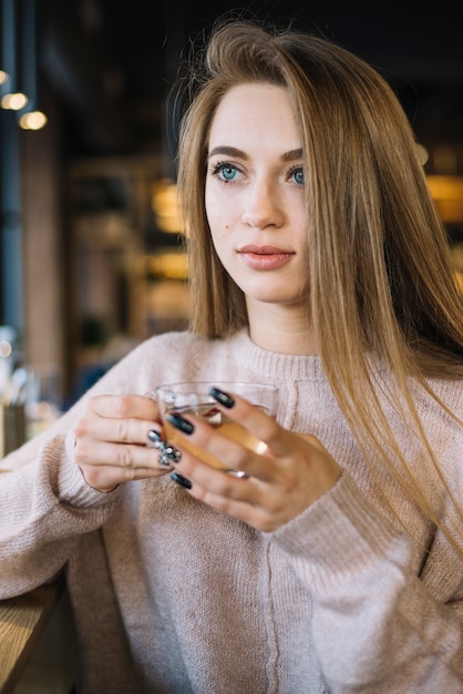 Elegante junge durchdachte Frau mit Cup des Getränks im Café