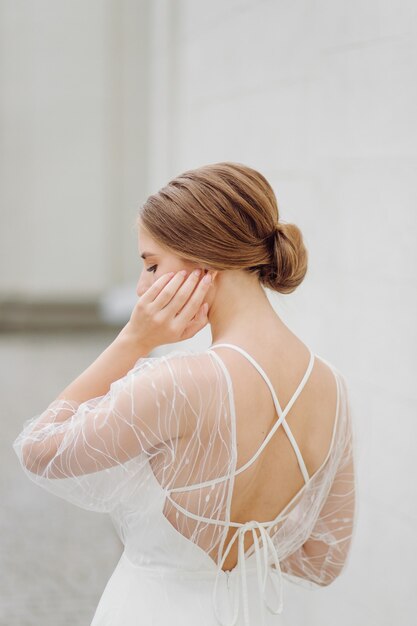 Elegante junge Frau im modischen weißen Kleid steht in der Nähe der Wand