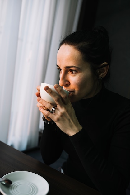 Kostenloses Foto elegante junge frau mit becher des getränks am tisch