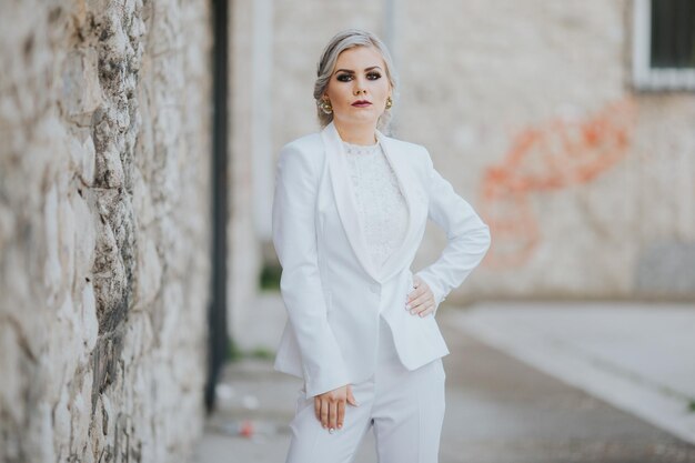 Elegante, modische kaukasische Frau in einem hübschen weißen Anzug und Hosen, die für ein Mode-Fotoshooting posieren