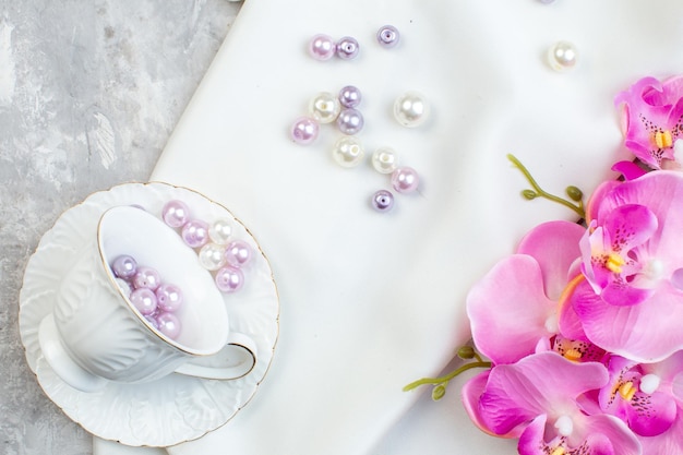 Elegante tasse in der draufsicht mit schönen perlen und blumen auf weißem oberflächenbild horizontale weibliche glasfarbenschönheit