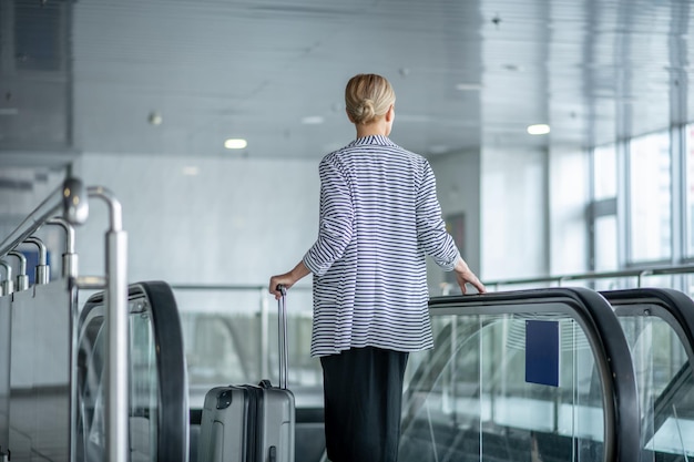 Elegante Touristin mit dem Trolley-Koffer auf der Rolltreppe