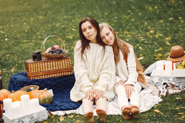 Elegante und stilvolle Mädchen, die in einem Herbstpark sitzen