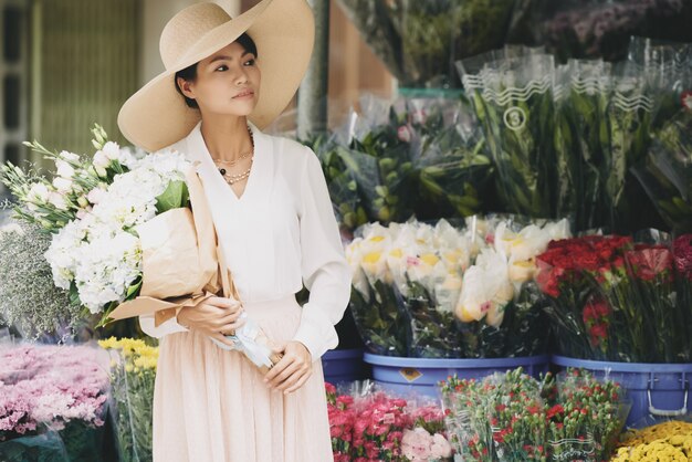 Elegante wohlhabende asiatische Dame mit dem großen Blumenstrauß, der außerhalb des Blumenladens wartet