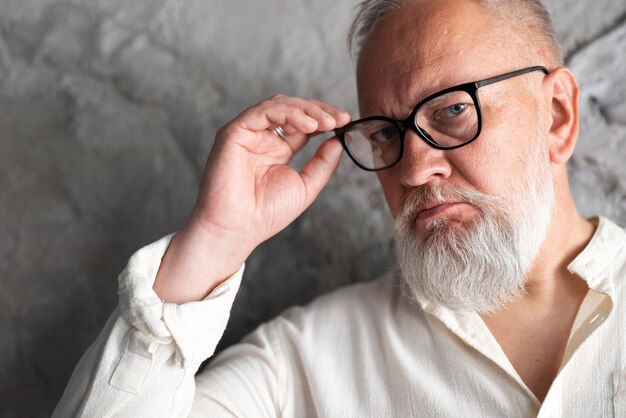 Eleganter älterer Mann, der in weißem Hemd und Brille posiert