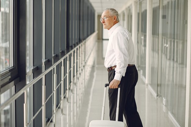 Eleganter alter Mann am Flughafen mit einem Koffer