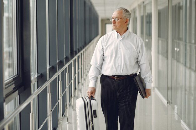 Eleganter alter Mann am Flughafen mit einem Koffer