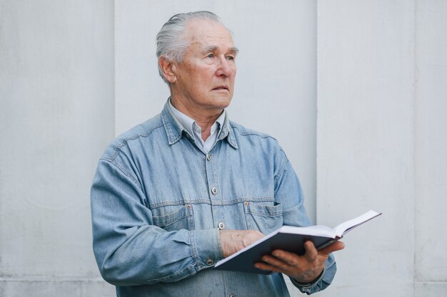 Eleganter alter Mann, der auf grauem Hintergrund mit einem Buch steht