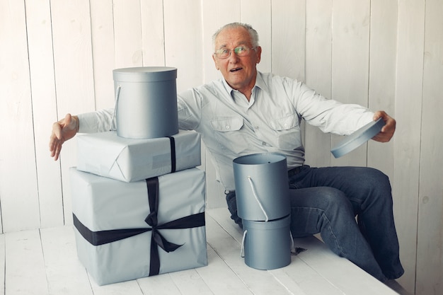 Eleganter alter Mann, der zu Hause mit Weihnachtsgeschenken sitzt